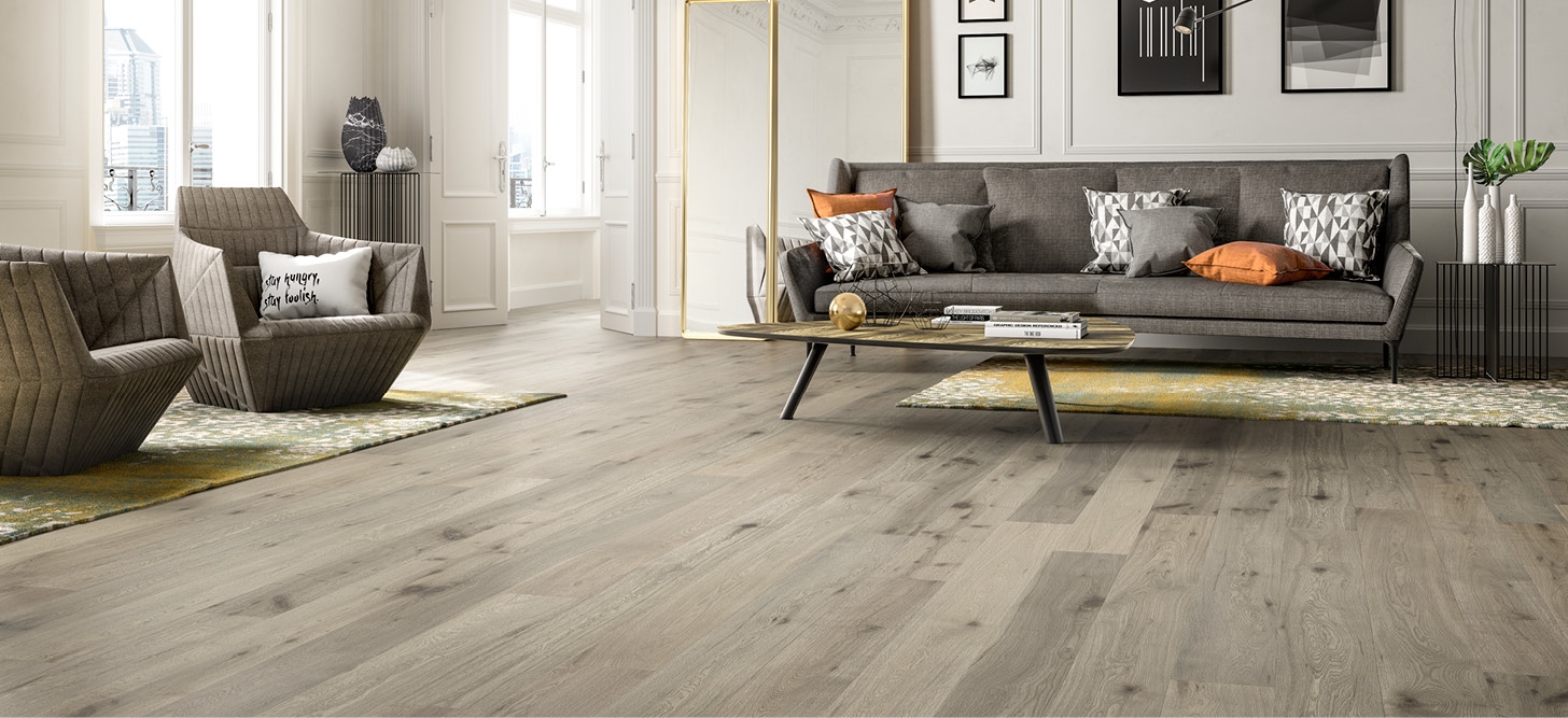 Salón con suelo de madera de tono claro, sofá gris y butacas