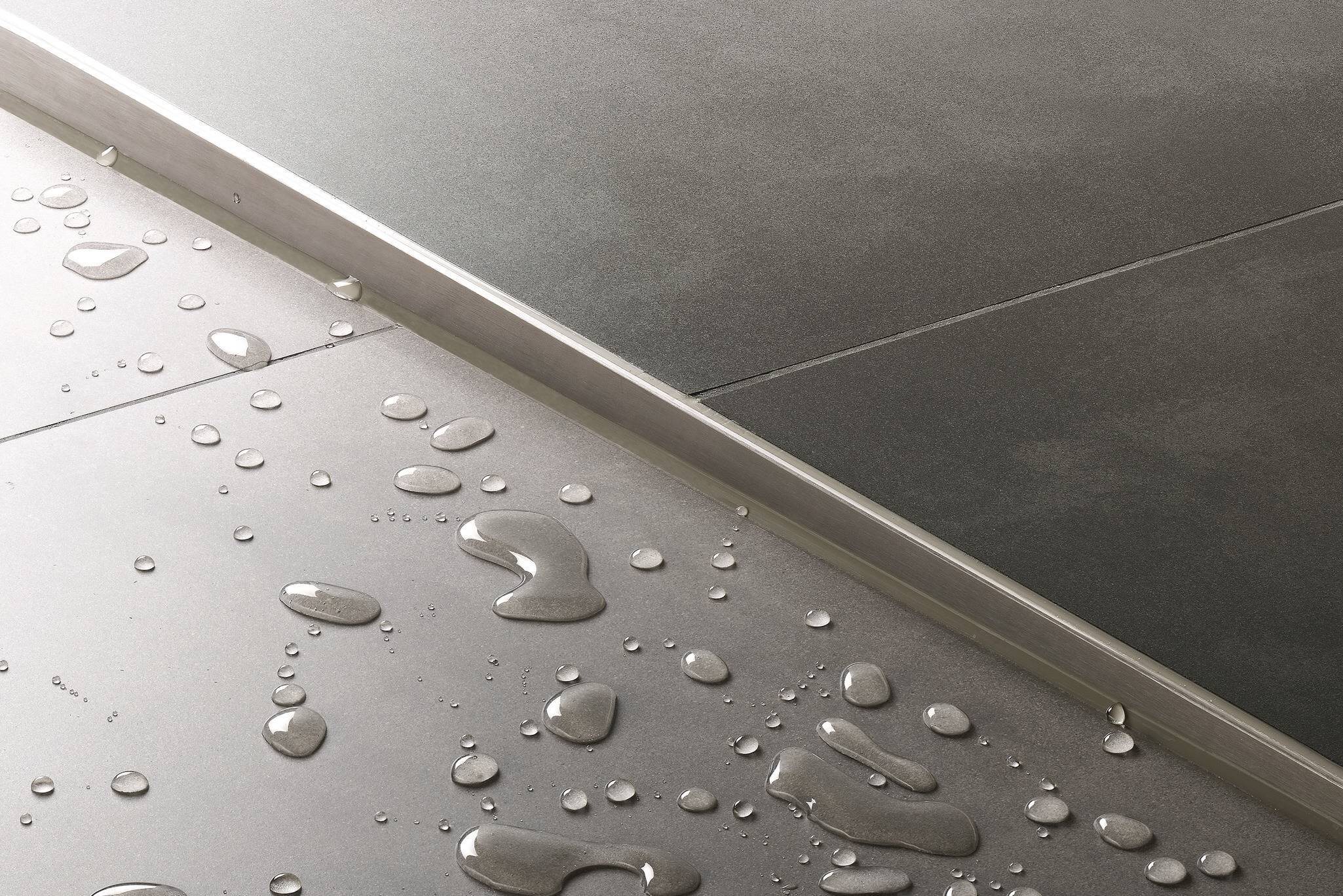 Stainless steel profile at the shower tray transition, with water droplets on the stoneware