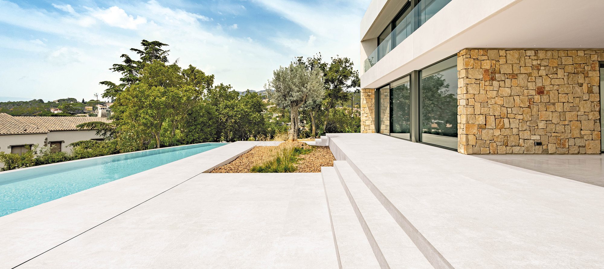 Terraza de gran formato porcelánico junto a una piscina infinita, con la casa al fondo