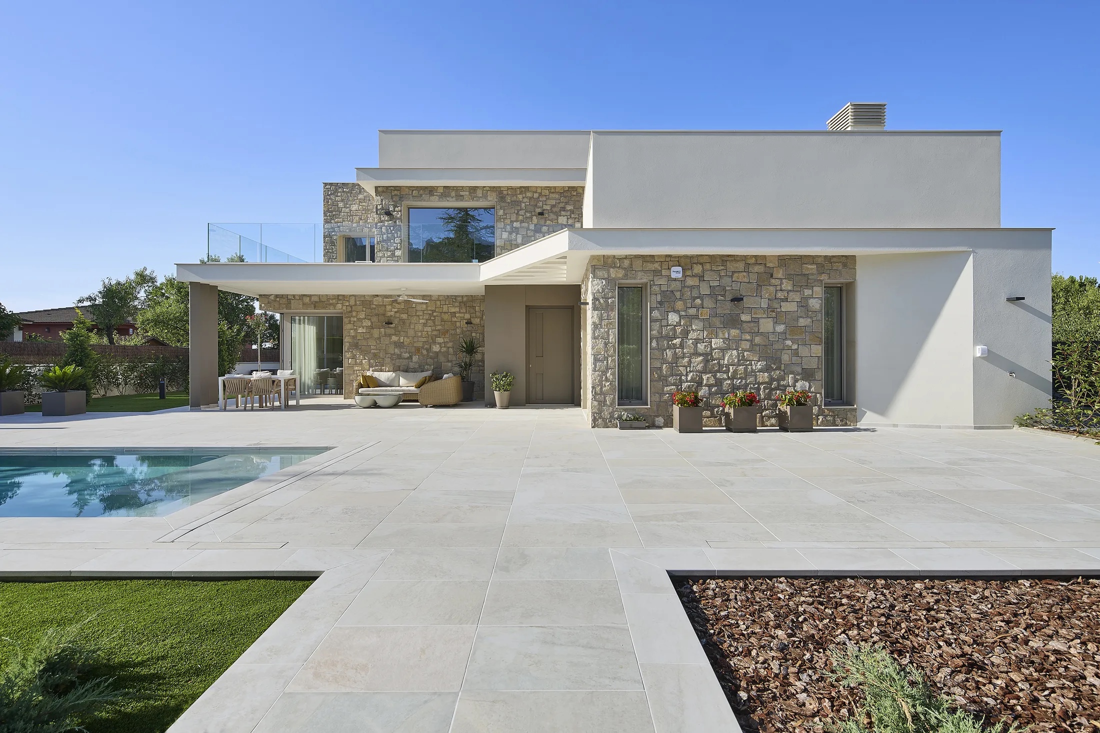 Terraza de porcelánico crema de gran formato junto a una villa de piedra